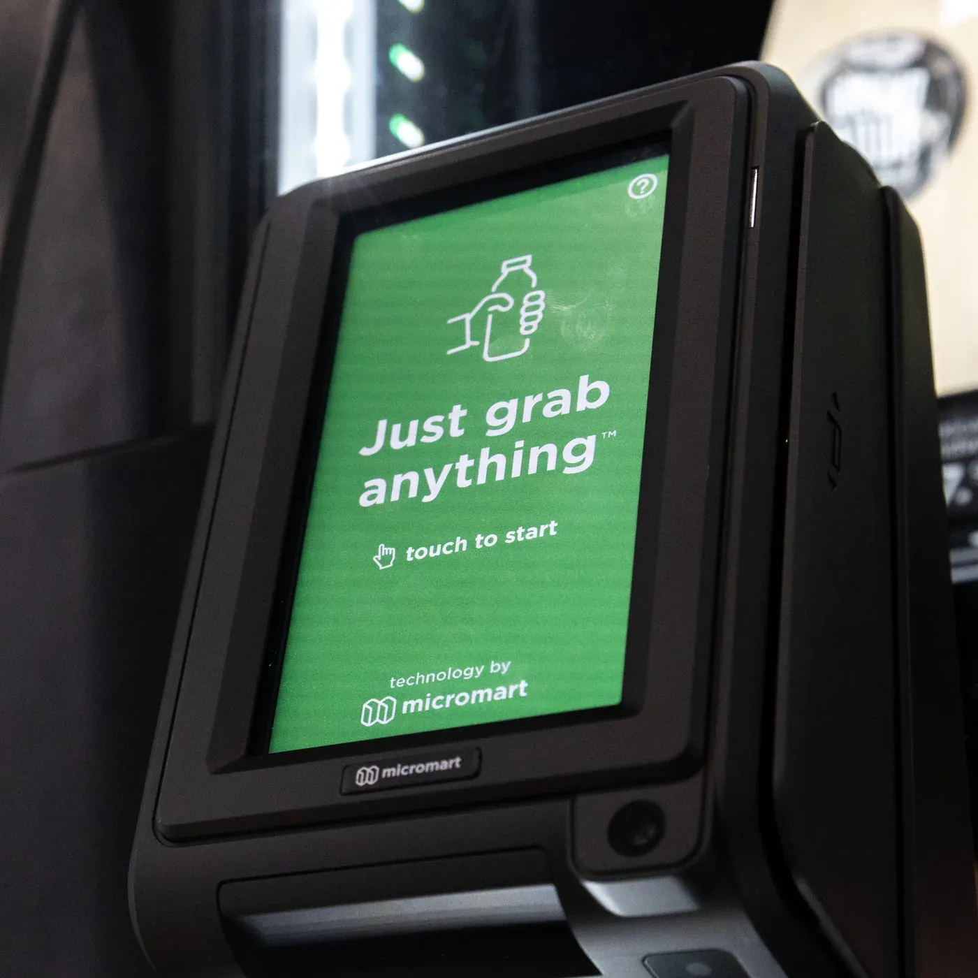 The reader on a smart cooler door, its screen lit green and reading "just grab anything — touch to start".